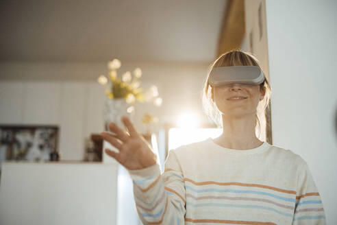 Lächelnde Frau mit Virtual-Reality-Headset gestikuliert zu Hause - JOSEF13645
