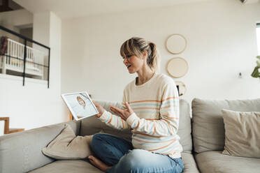 Schwangere Frau, die zu Hause auf dem Sofa sitzend mit einem Arzt über einen Tablet-PC spricht - JOSEF13648