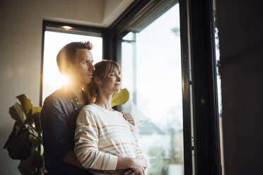 Expectant couple standing together near glass door at home - JOSEF13661