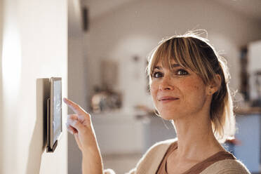 Lächelnde Frau, die eine Smart-Home-App auf einem Tablet zu Hause benutzt - JOSEF13673