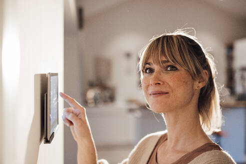 Smiling woman using smart home app on tablet at home - JOSEF13673