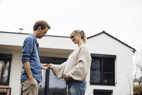 Lächelnde schwangere Frau hält Hand mit Mann vor einem Haus - JOSEF13684