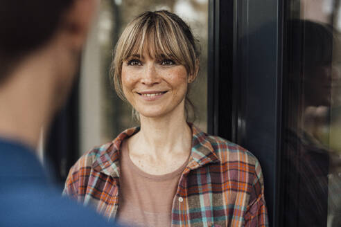 Smiling woman wearing plaid shirt looking at man - JOSEF13691