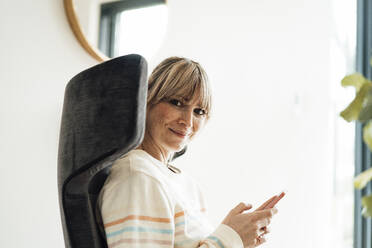 Lächelnde Frau sitzt auf einem Stuhl mit Smartphone - JOSEF13729
