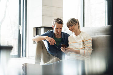Expectant couple sharing smart phone sitting at home - JOSEF13731