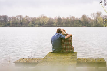 Romantic couple sitting on jetty at lake - JOSEF13735