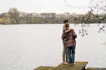 Man with arm around woman standing on jetty looking at lake - JOSEF13738