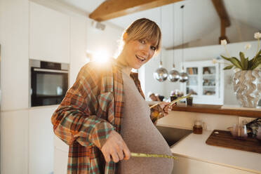 Glückliche schwangere Frau spielt mit Spargelstangen in der Küche zu Hause - JOSEF13757