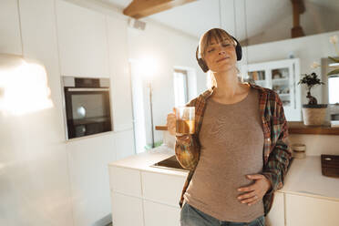 Pregnant woman touching belly listening to music through headphones at home - JOSEF13758