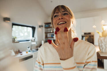 Happy woman with raspberries on fingers at home - JOSEF13759