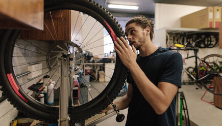Mann, der in einer Werkstatt an einem Fahrradrad arbeitet. Arbeiter, der ein Fahrrad in einer Werkstatt repariert. - JLPSF01693