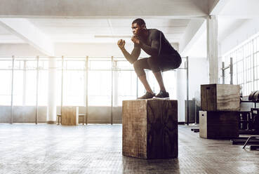 Ein Mann macht Kniebeugen auf einer Squatbox im Fitnessstudio. Ein Crossfit-Typ trainiert im Stehen auf einer hölzernen Squatbox. - JLPSF01699