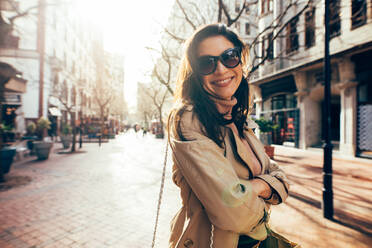 Lächelnde asiatische Frau steht mit verschränkten Armen auf der Straße in der Stadt. Stilvolles weibliches Modell mit Sonnenbrille auf der Straße in der Stadt. - JLPSF01704