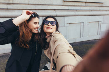 Beste Freundinnen machen ein Selfie draußen auf der Straße. Zwei junge Frauen machen ein Selbstporträt draußen in der Stadt. - JLPSF01706