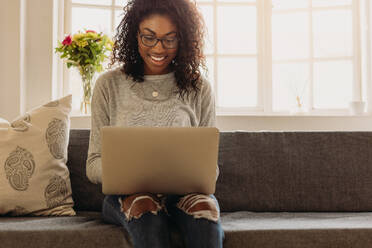 Smiling businesswoman sitting on sofa at home working on laptop computer. Woman managing business from home using laptop. - JLPSF01726