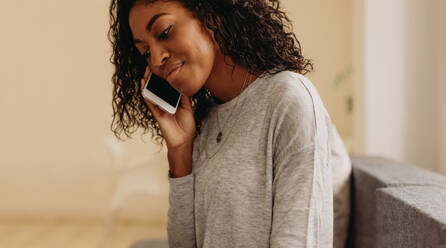 Close up of curly haired woman talking over mobile phone. Woman talking over mobile phone sitting at home. - JLPSF01729
