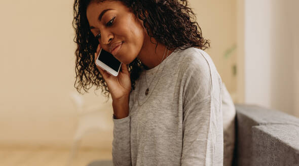 Nahaufnahme einer lockig behaarten Frau, die über ein Mobiltelefon spricht. Eine Frau, die über ein Mobiltelefon spricht, sitzt zu Hause. - JLPSF01729