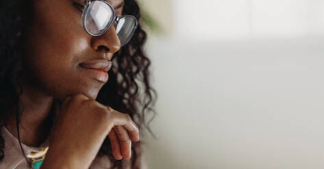 Close up of a curly haired businesswoman in spectacles with hand on chin. Side view of face of a woman with hand on chin. - JLPSF01781