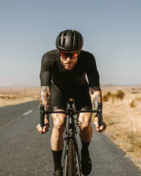 Porträt eines entschlossenen Radfahrers, der draußen auf der Straße Fahrrad fährt. Professioneller Sportler, der auf der Autobahn radelt. - JLPSF01784