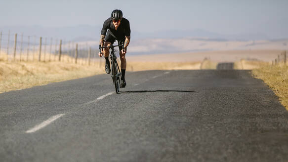 Sportler, der auf einer leeren Straße Rad fährt. Profi-Sportler, der auf einer Landstraße Rad fährt. - JLPSF01815