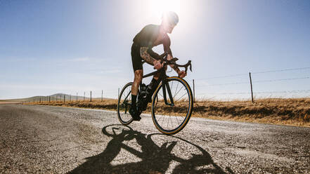 Tiefwinkelaufnahme eines männlichen Sportlers, der auf einer Landstraße Rad fährt. Ein professioneller Radfahrer trainiert hart an einem sonnigen Tag. - JLPSF01835
