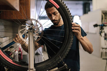 Mann, der in einer Werkstatt an einem Fahrradrad arbeitet. Arbeiter, der ein Fahrradrad in einer Werkstatt repariert. - JLPSF01838