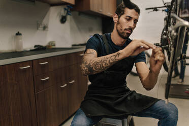 Man working on a bicycle in a repair shop. Worker fixing a bicycle brake wire in workshop. - JLPSF01839