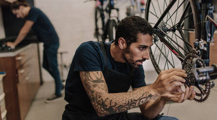 Ein Mann repariert ein Fahrrad in einer Werkstatt. Ein Arbeiter repariert eine Fahrradschaltung und eine Kette in einer Werkstatt. - JLPSF01840