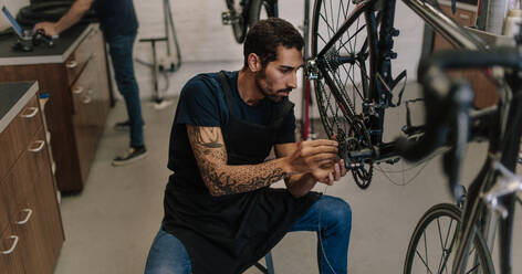 Ein Mann arbeitet an einem Fahrrad in einer Werkstatt. Ein Arbeiter repariert ein Fahrradbremskabel in einer Werkstatt. - JLPSF01841