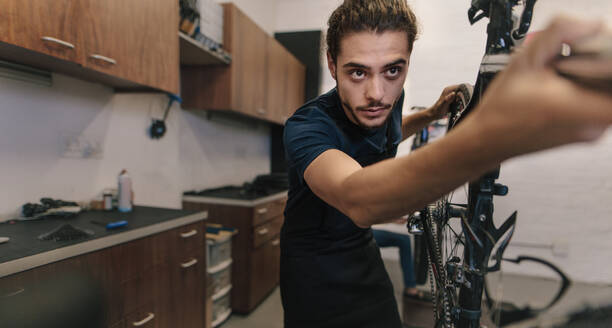 Arbeiter, der ein Fahrrad in einer Werkstatt repariert. Mann, der an einem Fahrrad in einer Werkstatt arbeitet. - JLPSF01847