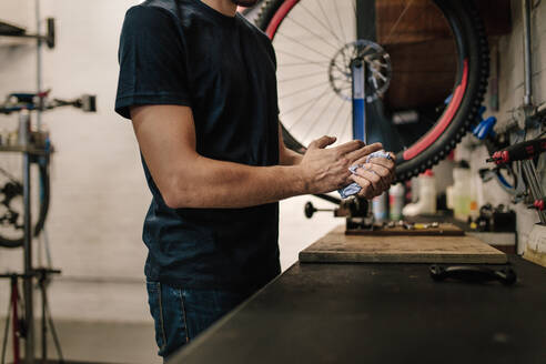 Arbeiter reinigt seine Hände nach der Fahrradreparatur in einer Werkstatt. Ausschnitt eines Mechanikers, der in einer Fahrradwerkstatt arbeitet. - JLPSF01853