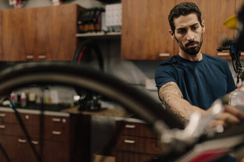 Arbeiter, der in einer Werkstatt ein Fahrrad repariert. Ein Mann arbeitet an der Befestigung eines Rades an einem Fahrrad. - JLPSF01854