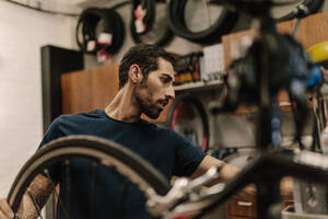 Arbeiter, der in einer Werkstatt ein Fahrrad repariert; Mann, der ein Rad an einem Fahrrad befestigt. - JLPSF01856