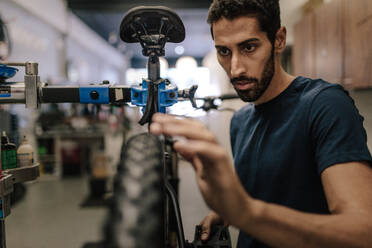 Worker repairing a bicycle at workshop. Man aligning the wheel of a bicycle in a repair shop. - JLPSF01857