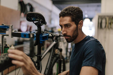 Arbeiter, der ein Fahrrad in einer Werkstatt repariert. Mann, der das Rad eines Fahrrads in einer Werkstatt ausrichtet. - JLPSF01858