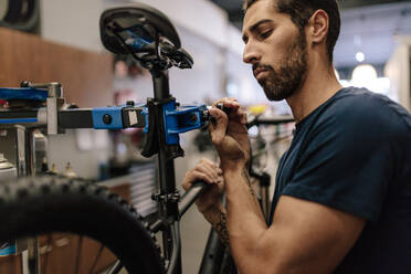 Worker repairing a bicycle at workshop. Man fixing a bicycle to a holding stand in a repair shop. - JLPSF01859