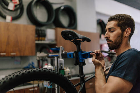 Arbeiter, der ein Fahrrad in einer Werkstatt repariert; Mann, der ein Fahrrad an einem Ständer in einer Werkstatt befestigt. - JLPSF01860