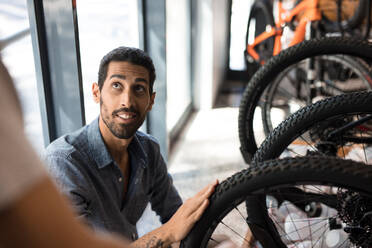 Lächelnder Mann in einer Fahrradwerkstatt posiert. Fahrradladenbesitzer mit neuen Fahrrädern in der Werkstatt. - JLPSF01863