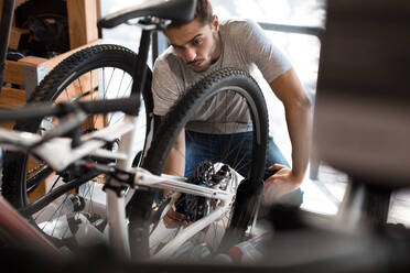 Mann, der ein Fahrradrad auf seine Ausrichtung überprüft. Mechaniker, der in einer Werkstatt ein Fahrrad repariert. - JLPSF01865