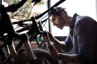 Mechanic inspecting a bicycle shock absorbers inside a showroom. Man at a bicycle showroom making repairs. - JLPSF01868