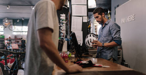 Mann an der Kasse, der einen Fahrradhelm verkauft. Besitzer eines Sportgeschäfts, der eine Rechnung für den Verkauf eines Helms am Computer ausstellt. - JLPSF01869