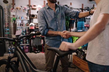 Beschnittene Aufnahme eines Ladenbesitzers, der einem Kunden nach dem Verkauf eines Fahrrads die Hand schüttelt. - JLPSF01872