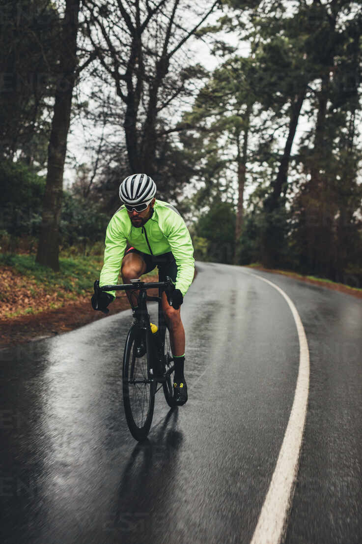 Male cyclist riding bike on countryside highway on a rainy day