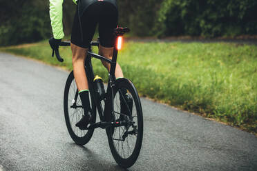 Rückansicht eines männlichen Radfahrers, der auf einer nassen Straße auf dem Lande übt. Professioneller Radfahrer, der auf offener Straße Fahrrad fährt. - JLPSF01896