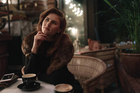 Junge Frau sitzt im Café mit einer Tasse Kaffee auf dem Tisch und schaut weg. Kaukasische Frau verbringt ihre Freizeit im Café. - JLPSF01903