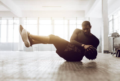 Athletischer Mann bei einer Bauchmuskelübung auf dem Boden. Mann beim Crossfit-Workout mit einem Medizinball im Fitnessstudio. - JLPSF01906