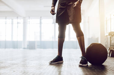 Ein sportlicher Mann steht im Fitnessstudio neben einem Medizinball. Nahaufnahme der unteren Hälfte eines Mannes, der im Fitnessstudio trainiert. - JLPSF01907