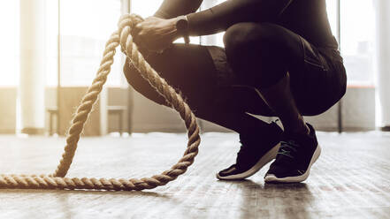 Close up of a man sitting on his toes holding a pair of battle ropes for workout. Crossfit guy at the gym working out with fitness rope. - JLPSF01911