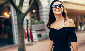 Lächelnde asiatische Frau, die auf der Straße in der Stadt spazieren geht. Stilvolles weibliches Modell mit Sonnenbrille, das auf der Straße in der Stadt spazieren geht. - JLPSF01913