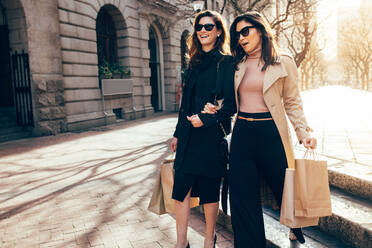 Stylish Frauen Freunde zu Fuß auf der Straße der Stadt mit Einkaufstaschen. Weibliche Käufer tragen Einkaufstaschen beim Gehen entlang der Straße. - JLPSF01924